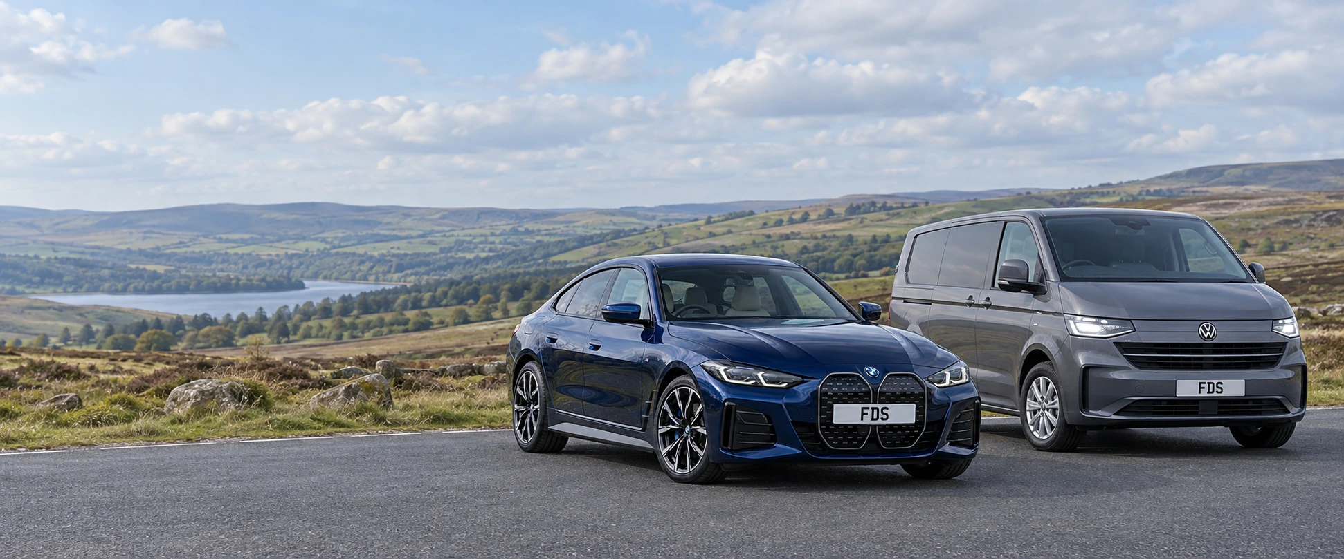 A blue BMW i4 and a grey Volkswagen Transporter at a countryside viewpoint.