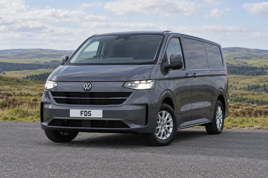 A grey Volkswagen Transporter panel van on tarmac beside open countryside.